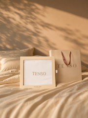TENSO presentation box and carrier bag resting on a made bed, leaf shadows on the wall behind